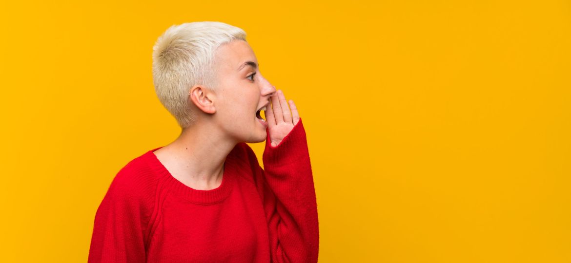 Teenager girl with white short hair over yellow wall shouting with mouth wide open