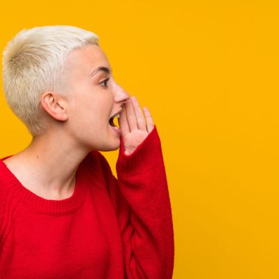 Teenager girl with white short hair over yellow wall shouting with mouth wide open